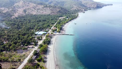 Rugged-mountain-shoreline-with-white-sandy-beach-and-turquoise-ocean-and-coral-reefs-on-remote-tropical-island,-Atauro-Island-in-Timor-Leste,-static-aerial-drone