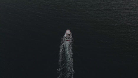 Commercial-fishing-boat-heading-out-into-the-open-ocean,-overhead-drone-view
