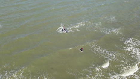 Aerial-footage-a-man-on-a-Jet-Ski,-another-wading-towards-the-shore