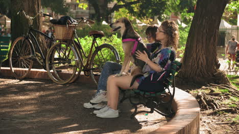 Scene-of-women-sitting-on-park-bench,-one-with-dog-on-her-lap