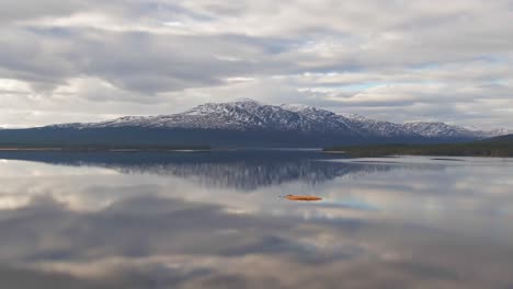 Parallax-Drone-Shot-Of-Swedish-Lake-With-Snowcapped-Mountains-and-Cloudy-Sky