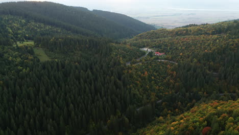 Aerial-Push-of-Early-Autumn-Green,-Orange-and-Yellow-Forest-in-a-Hilly-Terrain