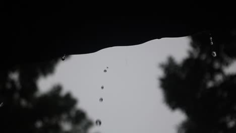 Rain-Water-Droplets-Falling-from-Rooftop-After-Rainstorm-in-Silhouette-Background-with-Slow-Motion-Looking-Upward