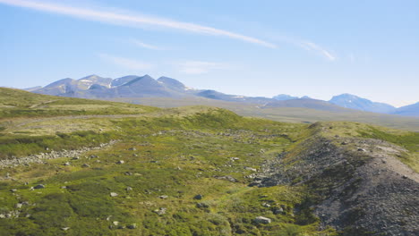 Felsige-Grüne-Felder-Mit-Bergen-Und-Blauem-Himmel-Im-Hintergrund-Im-Rondane-Nationalpark,-Norwegen