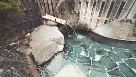 Water-Coming-Out-From-Bamboo-Pipe-Into-An-Outdoor-Onsen-In-Gifu,-Japan