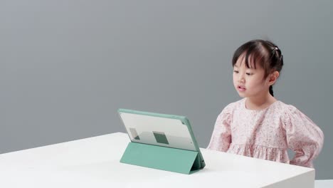 Child-using-digital-tablet-sitting-near-the-table-to-watch-cartoon