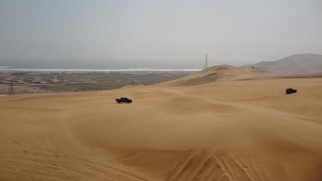 Aerial-view-around-trucks-driving-over-dunes-in-cloudy-Ica,-Lima,-Peru---circling,-drone-shot