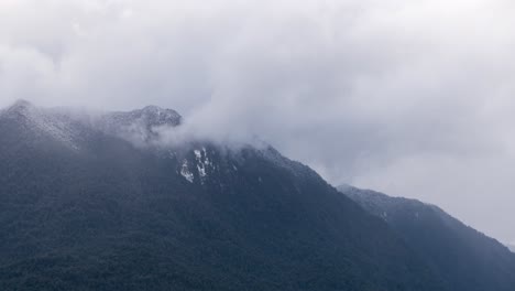 Lapso-De-Tiempo-De-Cimas-De-Montañas-Llenas-De-Nieve-Con-Nubes-Pasando-Por-Encima-En-Hornopiren,-Chile