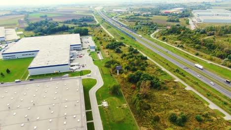 Big-logistics-terminal-in-countryside-near-highway,-Delivery-center-traffic-on-the-highway-aerial-shot