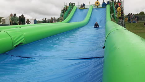 English-Woman-Slides-On-A-Board-At-Giant-Slip-And-Slide-In-Cornwall,-UK