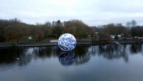 Luke-Jarram-floating-earth-art-exhibit-aerial-view-Pennington-flash-lake-nature-park-rising-pull-back