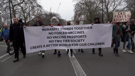 Los-Manifestantes-Contra-Las-Vacunas-Marchan-Con-Una-Pancarta-Blanca-Que-Dice:-&quot;La-Humanidad-Se-Mantiene-Unida,-Sin-Vacunas-Forzadas,-Sin-Pasaportes-De-Vacunas,-Sin-Sociedad-De-Dos-Niveles,-Crea-Un-Mundo-Mejor-Para-Nuestros-Niños&quot;.