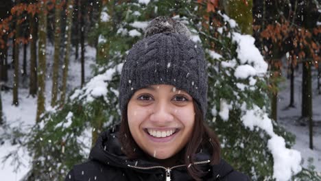 Beautiful-Asian-woman-looking-towards-camera-and-smiles-in-forestry-area-during-snowfall