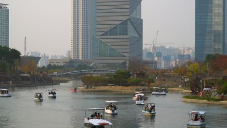 Korean-people-riding-family-paddle-boats-in-Songdo-Central-Park-with-G-Tower-on-background-at-sunset-in-Incheon,-South-Korea