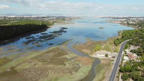Drone-shot-of-swampland-and-river-beside-road-with-cars-during-sunny-day-in-Seixal,Portugal