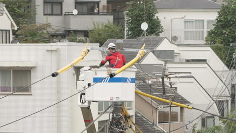 Licensed-Electrician-In-Lift-Bucket-Working-On-Power-Line-With-Covered-With-Yellow-Line-Guard-In-Tokyo,-Japan