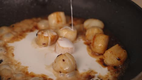 Close-up-cooking-shot-of-chef-adding-coconut-milk-into-frying-pan-with-delicious-fresh-seafood-scrallops-bubbling,-browning-and-cuddling-in-high-heat