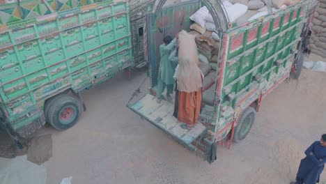 Pakistanische-Männliche-Arbeiter-Heben-Säcke-Mit-Reis-Auf-Die-Ladefläche-Eines-Lastwagens-In-Der-Fabrik