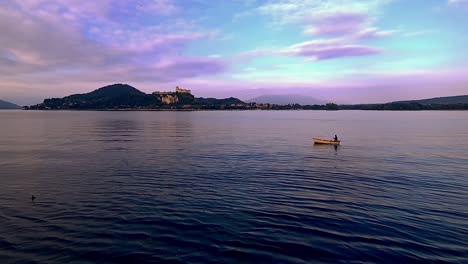 Evocative-wide-angle-pov-of-small-fishing-boat-with-fisherman-rowing-in-lake-waters-of-Maggiore-lake-in-Italy