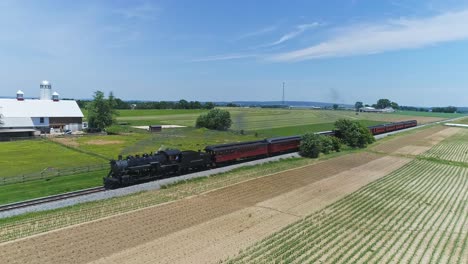 An-Aerial-Ride-Along-View-of-a-Steam-Engine-Puffing-Smoke-and-Steam-with-Passenger-Coaches-Traveling-on-a-Single-Track-Fertile-Farmland-and-Countryside-With-a-Farmer-Working-in-the-Background
