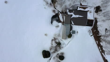 Expensive-modern-house-of-frozen-lakeside-in-forestry-area-during-winter-season,-aerial-top-down-view