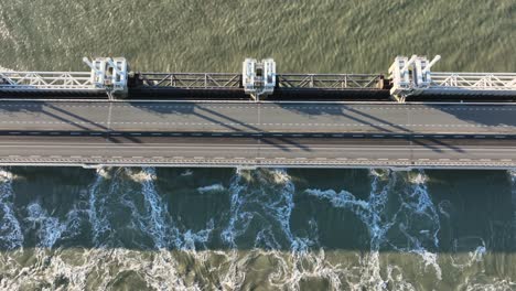 Aerial-vertical-tilting-shot-of-water-flowing-through-opened-sluices-on-the-Eastern-Scheldt-storm-surge-barrier-in-Zeeland,-the-Netherlands,-on-a-sunny-day