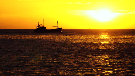Silhouette-of-fishing-boat-returning-home-during-golden-sunset-time,-static-view