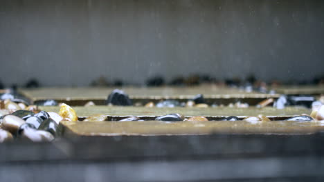 Slow-motion-shot-of-rain-hitting-an-outdoor-garden-pebbles-with-the-raindrops-splashing-at-200fps