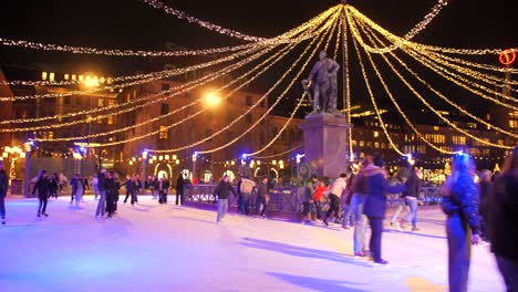 Many-people-skating-on-colorful-ice-skating-rink-at-night-with-beautiful-lights-during-christmas-in-Stockholm,-Sweden