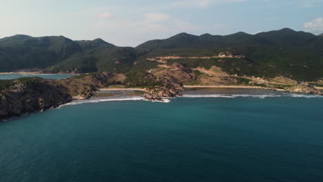 Hermoso-Mar-Azul-Claro-Que-Termina-Suavemente-En-Las-Hermosas-Playas-De-Arena-De-La-Bahía-De-Vinh-Hy-En-Vietnam-Con-Las-Altas-Montañas-Verdes-En-El-Fondo