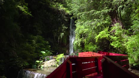 Waterfall-streaming-down-near-red-wooden-deck-surrounded-by-woods-in-Termas-Geometricas-hot-spring-complex,-Coñaripe,-Chile