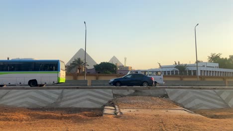 Traffic-driving-on-road-in-Egypt-at-sunset,-Great-Pyramids-of-Giza-in-background