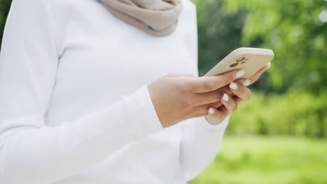 Frau-Mit-Hijab-Benutzt-Ihr-Telefon-Und-Schreibt-SMS,-Während-Sie-Im-Park-Spazieren-Geht,-Muslimisches-Mädchen-Mit-Smartphone