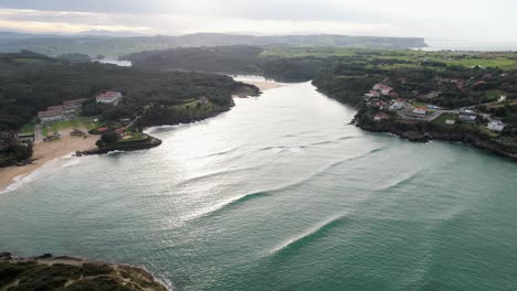 Huge-waves-from-the-Bay-of-Biscay-roll-into-the-beautiful-bay-in-Spain's-green-sparsely-populated-province-of-Cantabria-on-a-partly-cloudy-day