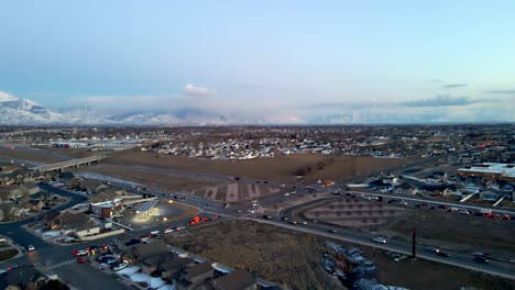 Traffic-along-a-highway-in-a-suburban-community-in-a-valley-beneath-the-snowy-Rocky-Mountains---descending-aerial-view