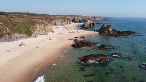 Praia-da-Samoqueira-Beach-near-Porto-Covo,-Alentejo,-West-Portugal---Aerial-Drone-View-of-Tourists-Chilling-at-the-Golden-Sandy-Beach