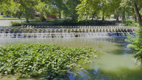 A-small-waterfall-at-a-city-park-with-beautiful-trees-on-a-sunny-afternoon