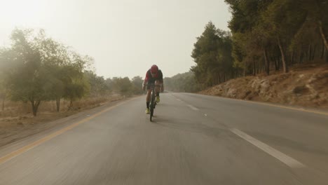 Cámara-Lenta-Dos-Ciclistas-De-Carretera-Profesionales-Cabalgando-Por-La-Carretera-Vacía-Del-Bosque-Y-El-Sol-Brilla-En-La-Cámara