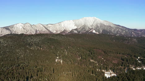 Left-to-right-aerial-tracking-shot-of-snowy-Postavarul-Massif,-Romania