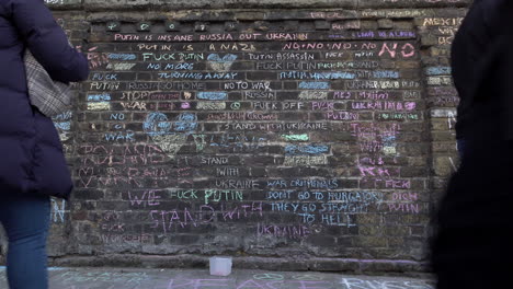 People-walk-past-the-wall-outside-the-Russian-embassy-that-has-anti-war-messages-drawn-on-in-chalk-during-a-protest-against-the-invasion-of-Ukraine
