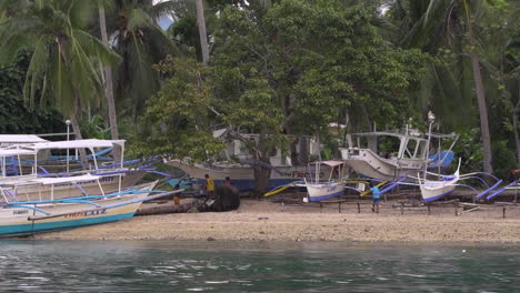 Long-Shot-Of-Kids-Playing-Under-The-Tree-With-Fishing-Boats,-Beach-Side