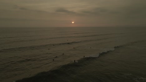 Dark-copper-sunset-aerial-as-evening-surfers-catch-small-shore-break