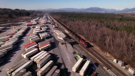 Aerial-tracking-shot-of-cargo-train-running-on-railway-along-Vancouver-shipping-terminal-in-Canada