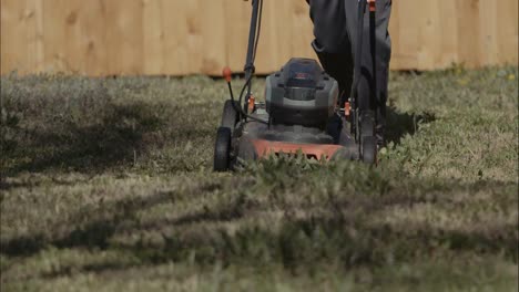 An-electric-mower-being-pushed-over-grass-and-weeds-towards-the-camera