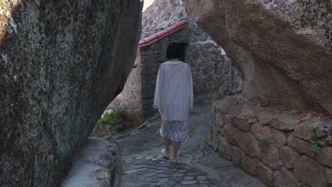 Back-view-of-unrecognizable-woman-walking-between-rocky-walls-of-Monsanto-historic-center,-Portugal
