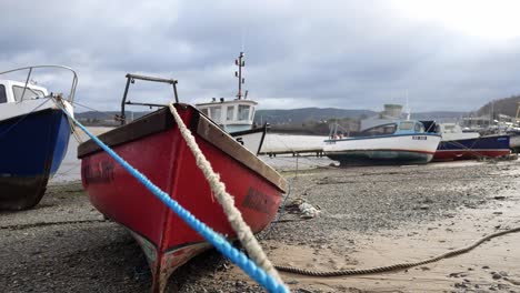 Empty-boats-moored-on-low-tide-pebble-waterfront-beach-North-Wales-fishing-harbour