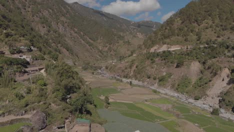 Beautiful-farming-village-farms-paddy-field-vegetables-growing-in-mountainous-valley-in-Kabayan-Benguet-Philippines-wide-aerial-approaching-right-trucking-revealing-valley-river-mountains-blue-sky