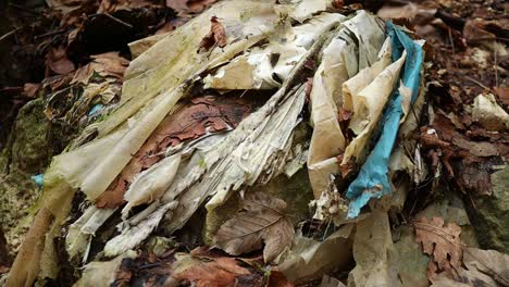 old-plastic-fabrics-among-the-leaves-in-the-forest,-close-up-shot