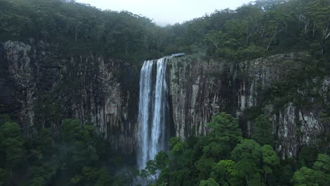 Panoramic-view-of-a-majestic-waterfall-spilling-down-a-tropical-rainforest-covered-mountain