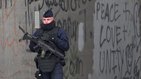 A-CRS-police-officer-armed-with-an-assault-rifle-stands-guard-in-front-of-graffiti-on-a-bridge-that-reads,-“Peace-+-love-+-unity”